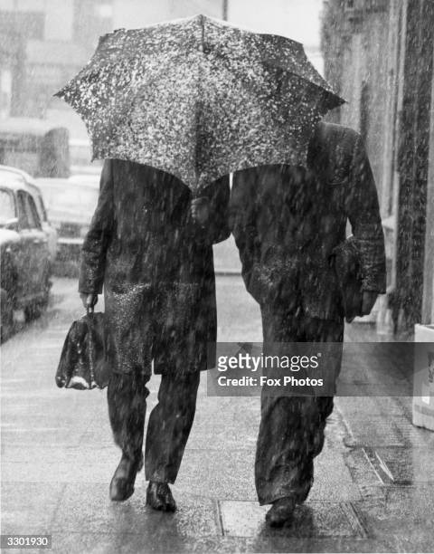 Two city gents, one caught without his overcoat walking in Farringdon Road, share an umbrella as snow falls across London.