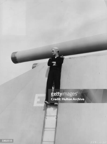 American actor Robert Montgomery , formerly Henry Montgomery perched on one of the big turrets aboard the US Colorado during the filming of...
