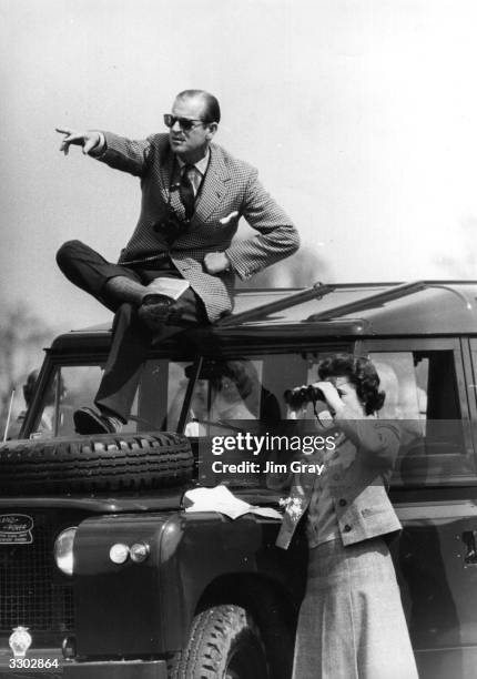 Prince Philip, Duke of Edinburgh seated on the roof of a Land Rover pointing out competitors at the Badminton Horse Trials to Queen Elizabeth II who...