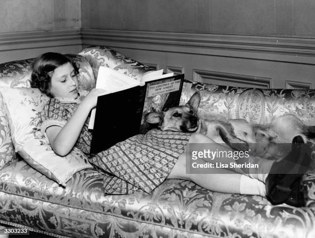 Princess Margaret Rose younger daughter of King George VI and Queen Elizabeth, reading on the sofa at Windsor Castle, accompanied by Jane the corgi.