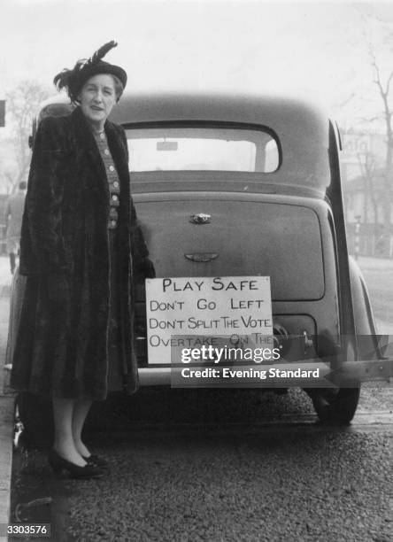 Lady standing by the rear of car with a sign stating 'Play safe, Don't go left, Don't split the vote, Overtake on the right' during the 1950 General...