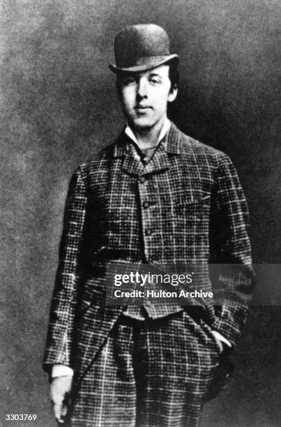 Irish playwright, novelist and wit Oscar Wilde , wearing a checked three-piece suit and bowler hat.