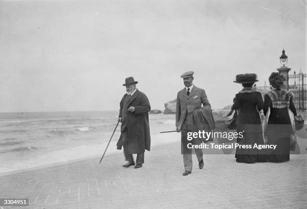 King Edward VII , who ascended the British throne in 1901, walks on the seafront at Biarritz with a companion.