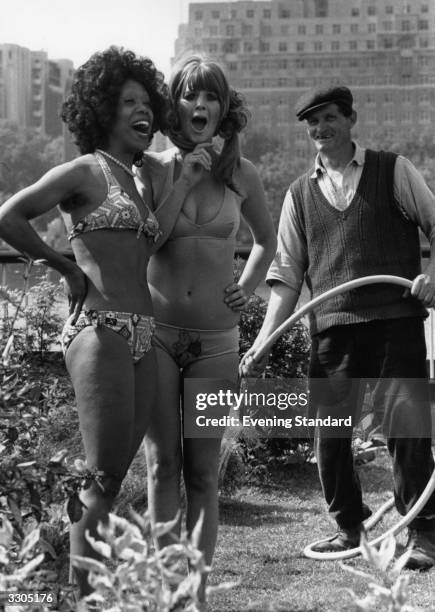 Two women modelling swimwear in a garden on London's South Bank, watched by a gardener with a hose.