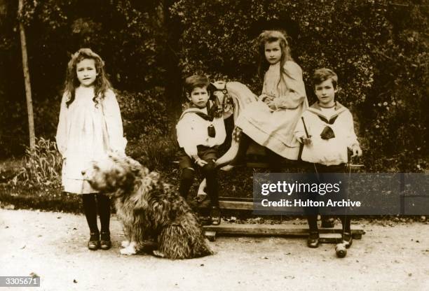 Four Edwardian children in a garden with their toys and a dog.