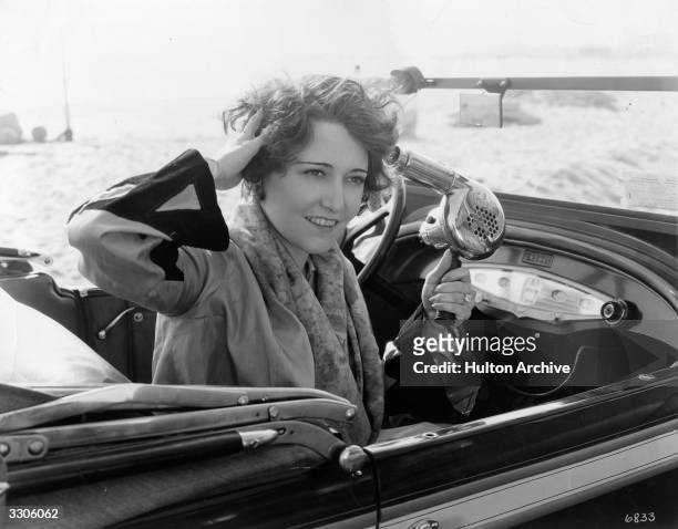 American actress Dorothy Sebastian using her hand-held hairdryer which operates from a battery on the dashboard of her car so that whenever she goes...