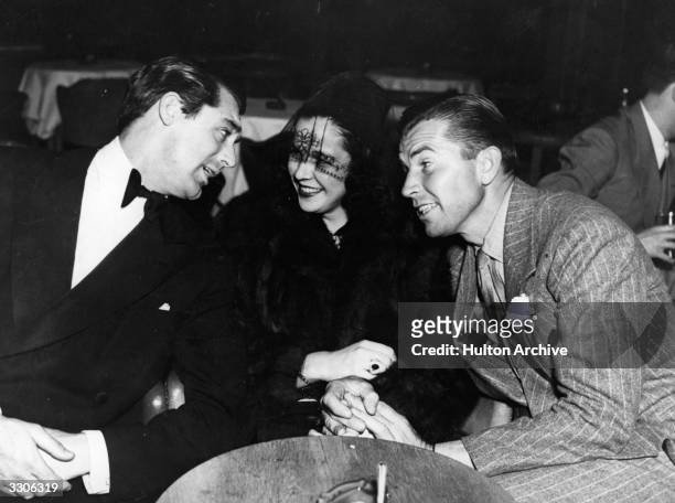 From left, English-born American actor Cary Grant talks with socialite and fashion designer Gloria Vanderbilt and actor Bruce Cabot .
