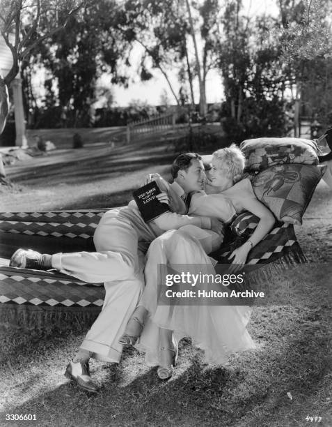 Robert Young and Joan Marsh, both MGM film stars, get some practice in the art of love on a hammock in a shady glen. Robert holds the book of...