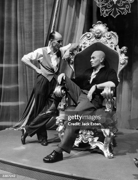 Yul Brynner chatting with costume designer Arthur Newman during the filming of 'Anastasia' at Elstree. The film, set in Paris, stars Ingrid Bergman...