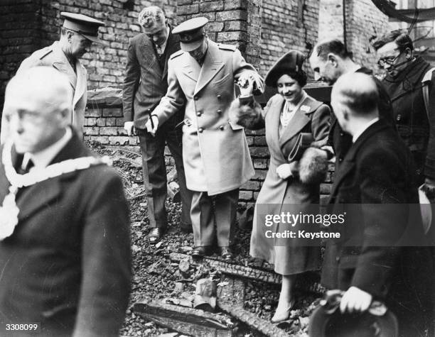 King George VI and Queen Elizabeth helping one another over debris during a visit to a bomb-damaged area in Salford, Lancashire.