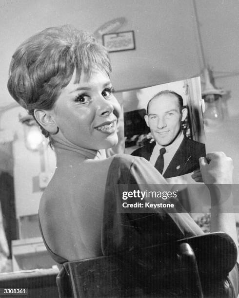 English actress Judy Carne holds a picture of her boyfriend racing driver Stirling Moss.