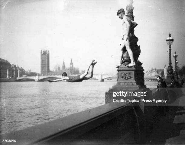 During an April heatwave boys are diving into the Thames, from a lamp-post on the Embankment at Vauxhall. Big Ben can be seen on the skyline.