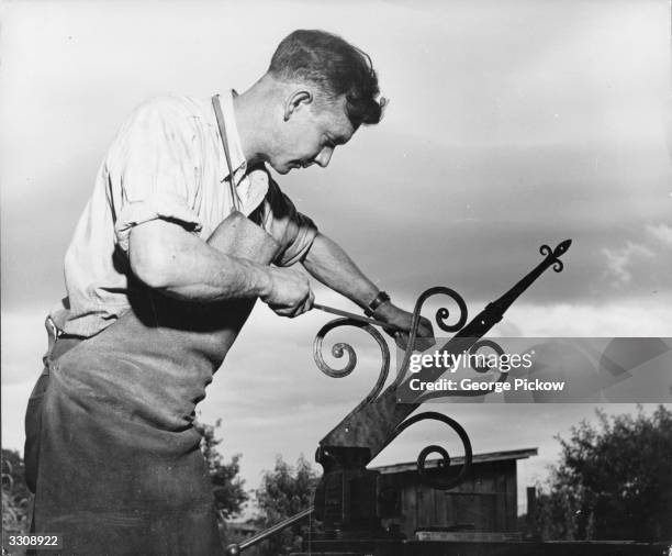 Worker filing down the finished surface of a wrought iron hinge plate after it has been hammered into shape.