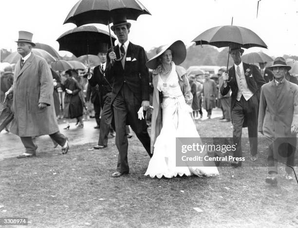 Racegoers at Ascot shelter under umbrellas from the rain.