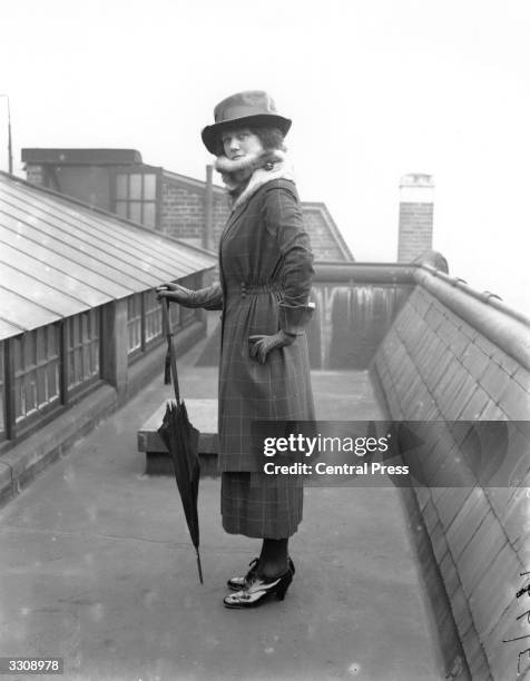 Model posing on a roof-top and wearing a ruched-waist suit from Burberry's, London, with fur collar and gauntlet gloves.