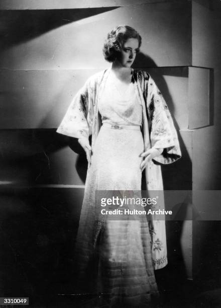 American actress Bette Davis, wearing an evening gown of chantilly lace with a mandarin wrap decorated with fine embroidery.