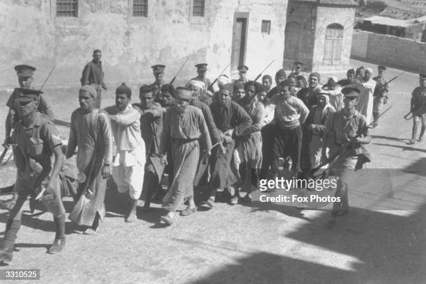 Line of prisoners, chained wrist to wrist, being taken to jail in Jerusalem during a period of curfew by the British mandate forces.