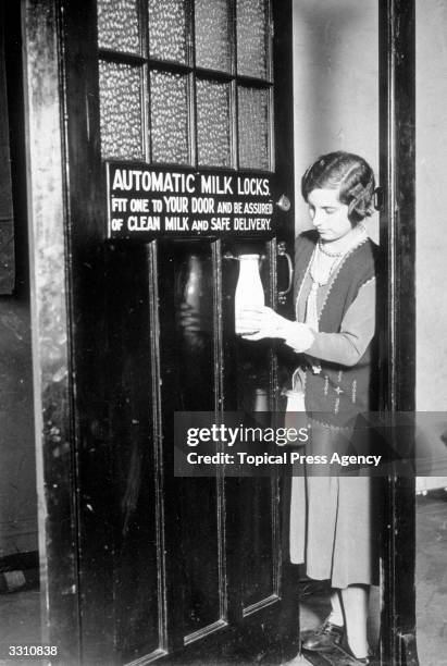 Woman unhooking a bottle of milk from an automatic milk lock, which was one of the exhibits at the Exhibition of Inventions at Central Hall,...