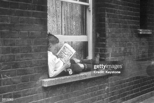 Young boy lying on a window ledge reading a comic.