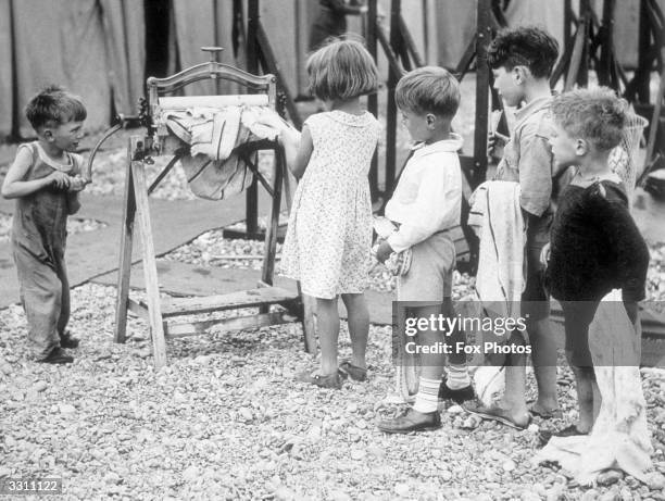 Young boy seen here turning the mangle as his friends queue up with their wet washing.