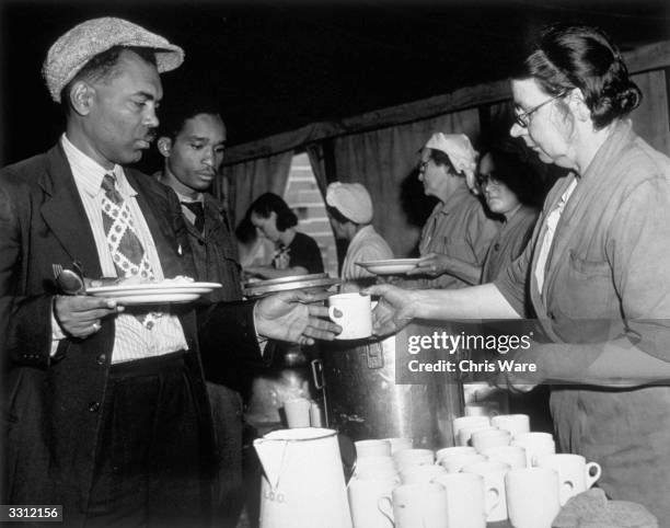 Jamaican men, who arrived in Britain on HMT Empire Windrush on 22nd June, collect a meal in a canteen marquee on Clapham Common to get a meal,...