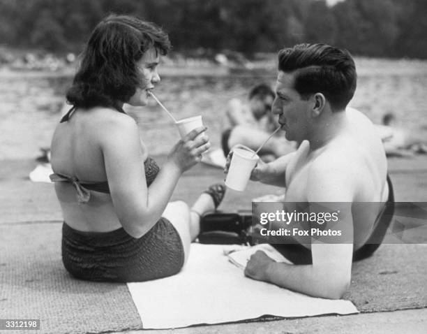 Couple of holidaymakers drinking through straws at Hyde Park Lido, London