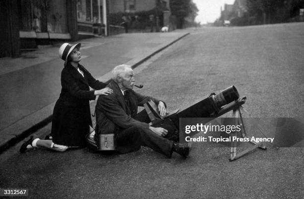 An amateur astronomer photographing an eclipse of the sun from the middle of a road, assisted by a schoolgirl.