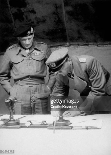 Field Marshal Bernard L. Montgomery watches General Kienzl, Chief of Staff to Field Marshal Busch, sign the surrender of the German land, sea and air...