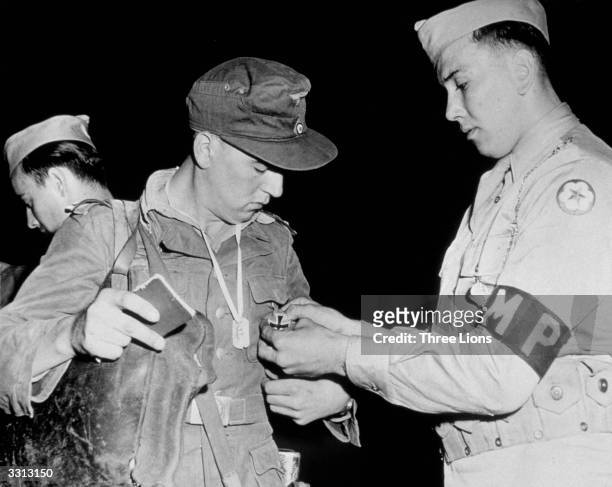 The Iron Cross is removed from the shirt of a German prisoner by an American Military Policeman. Medals were not worn by German captives.