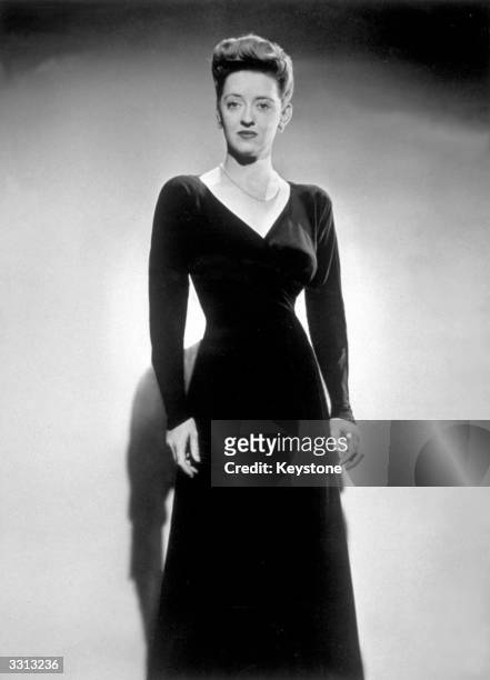 American actress Bette Davis wearing a black frost crepe dinner gown.