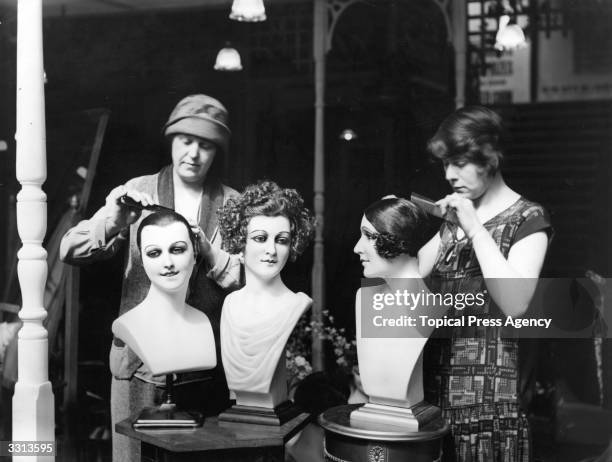 Two women demonstrating hairstyles on mannequin heads at the Drapery and Textile Exhibition at the Royal Agriculture Hall, London.