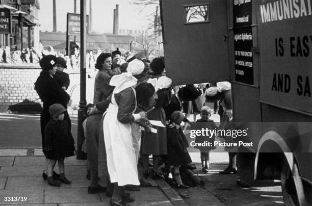 Mothers queue up with their children outside a medical van, which was set up to travel the area and immunise children against diphtheria. Original...
