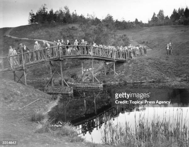 Spectators streaming across a bridge, on their way to the 18th green, during the Silver Tassie competition on the King and Queen's Golf course at...