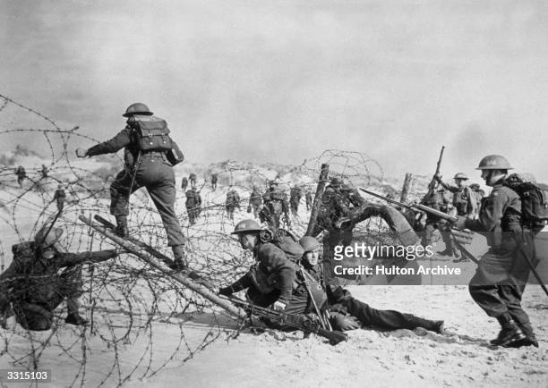 British soldiers negotiating a barbed wire defence during a seashore invasion exercise.