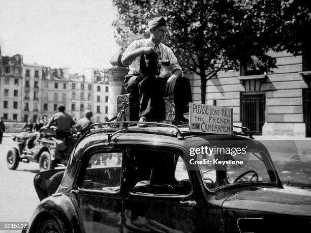 Newsreel cameraman filming from the top of his car, during the liberation of Paris, a notice beside him reads 'Please don't kill the French...