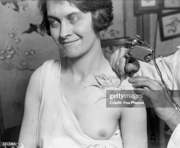 Woman having her shoulder tattooed with a goddess and a bird; a stiff upper lip seems necessary !