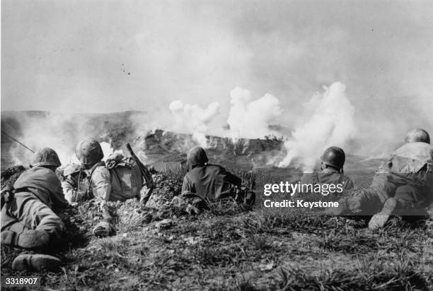 Marines of the 1st Division wait on the crest of a hill in southern Okinawa, as they watch phosphorous shells explode over Japanese soldiers dug into...