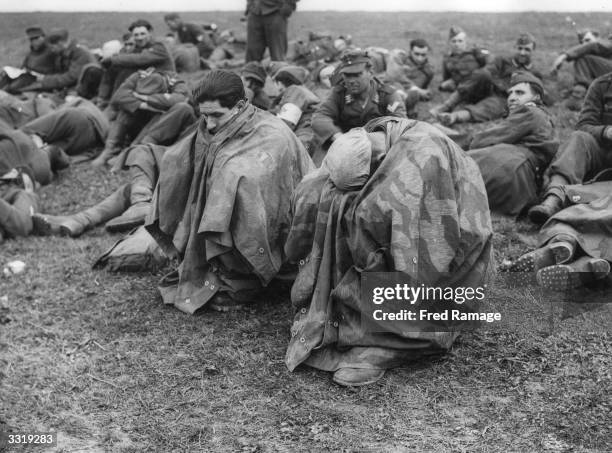 Tired and disconsolate German prisoners of war crouch under waterproof capes after their capture on the banks of the Rhine.