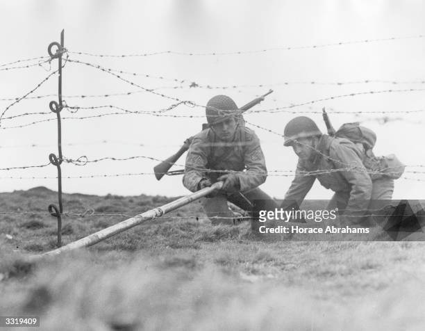 Combat engineers place a Bangalore torpedo under a barbed wire fence during exercises under battlefield conditions in the south of England.