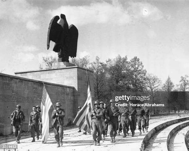 Soldiers of the 45th Division carrying US flags past a stone German eagle in the Luitpold Arena, Nuremberg, on V-Day. Now weed-covered, Hitler used...