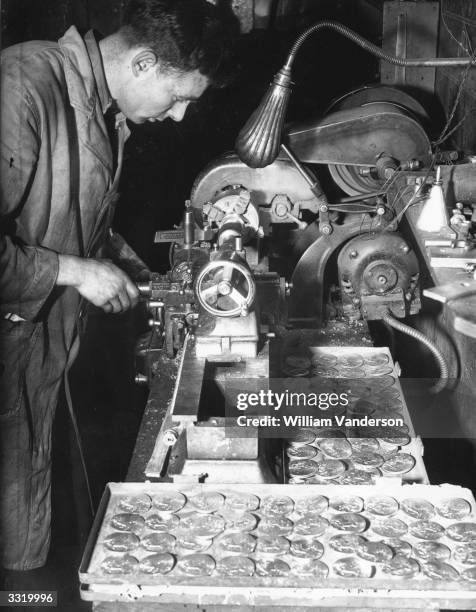 Man operating a press, stamping out Olympic Games medals at a London factory.