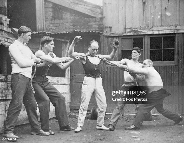 Tom Joyce, who claims to be Bristol's strongest man, showing his strength by four men pulling at a rope which is tied around his neck.