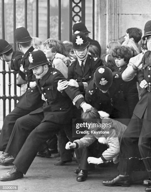 Police hold back a mass of young Beatles fans outside Buckingham Palace, London, where the pop group received MBE's.