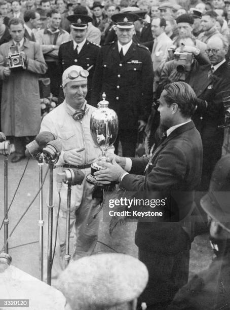 Italian racing driver Giuseppe Farina receives the trophy from Max Aiken after winning the International Trophy Race at Silverstone. He finished just...