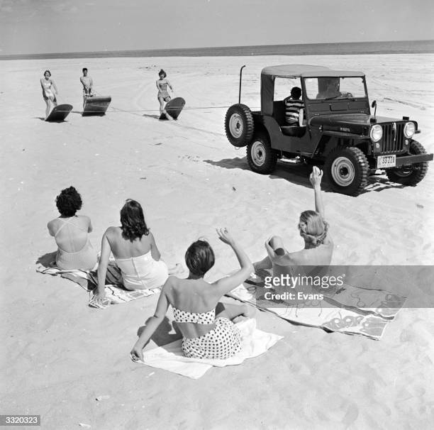 Sun bathers on a beach near Southampton, Long Island, USA, greet a trio of surfers pulled along the beach by an all-terrain vehicle.