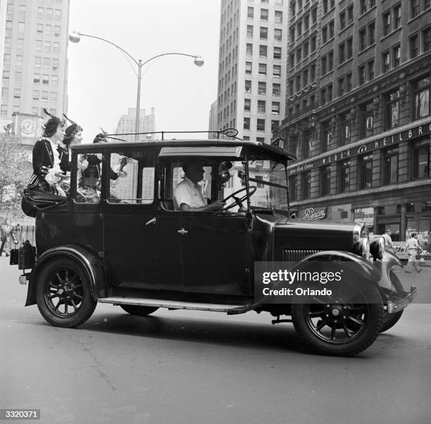 London taxicab, with three Scottish women wearing national costume riding on the back, in Herald Square, New York. It is one of the vintage cars...