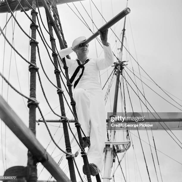 Young sailor in the rigging sailing ship 'Joseph Conrad', moored at Mystic, Connecticut, looking out to sea through a telescope. He is taking part in...