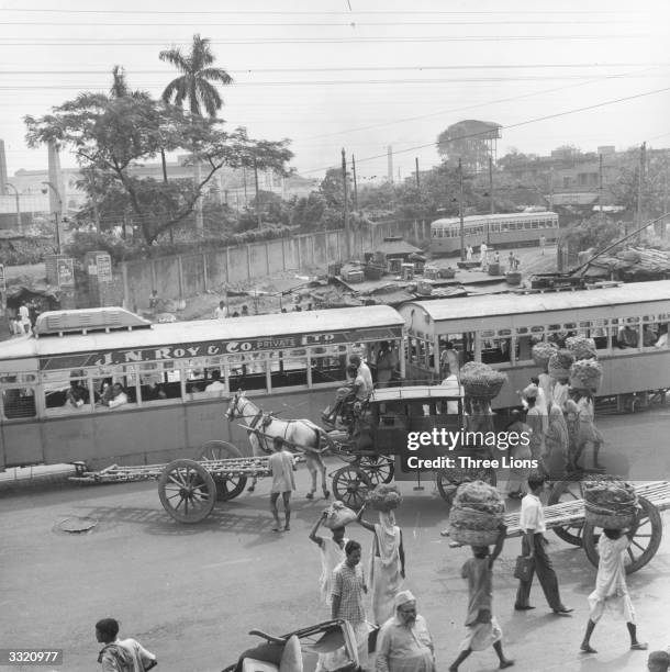 In a busy Calcutta street, trams mingle with horsedrawn carriages, pedestrians, wagons and jinrikishas or rickshaws.