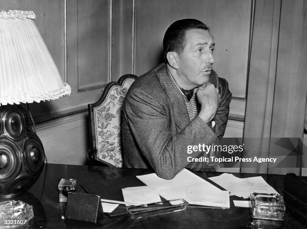 Artist and film producer Walt Disney , creator of Mickey Mouse, seated at a desk with paperwork in London.