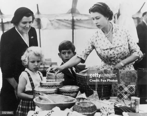 Queen Elizabeth II with Princess Anne, Prince Charles and their nurse, Helen Lightbody, at a stall during a Sale of Work event in Abergeldie Castle,...